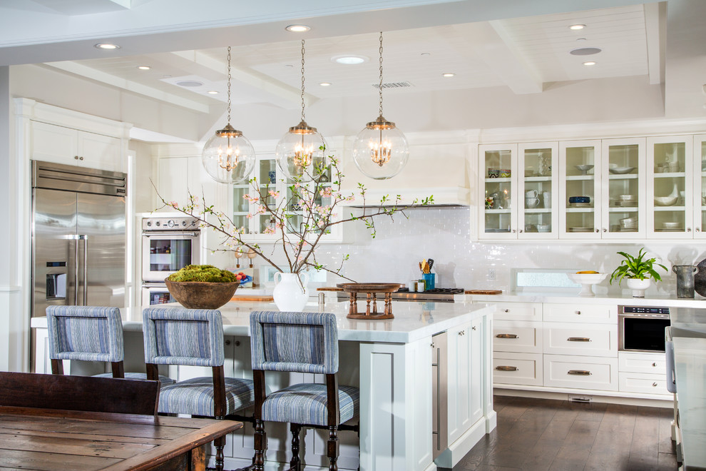 Example of a large transitional u-shaped dark wood floor open concept kitchen design in Orange County with a farmhouse sink, shaker cabinets, white cabinets, marble countertops, white backsplash, ceramic backsplash, stainless steel appliances and an island