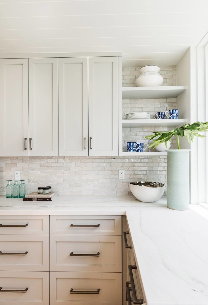 Bild på ett mellanstort maritimt vit vitt l-kök, med skåp i shakerstil, grå skåp, bänkskiva i kvarts, vitt stänkskydd, stänkskydd i keramik, rostfria vitvaror, ljust trägolv, en köksö och beiget golv
