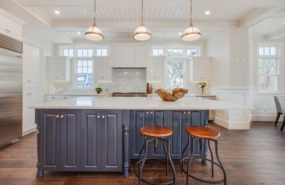 Foto på ett maritimt kök, med en rustik diskho, luckor med upphöjd panel, vita skåp, marmorbänkskiva, vitt stänkskydd, stänkskydd i marmor, rostfria vitvaror, mellanmörkt trägolv och en köksö