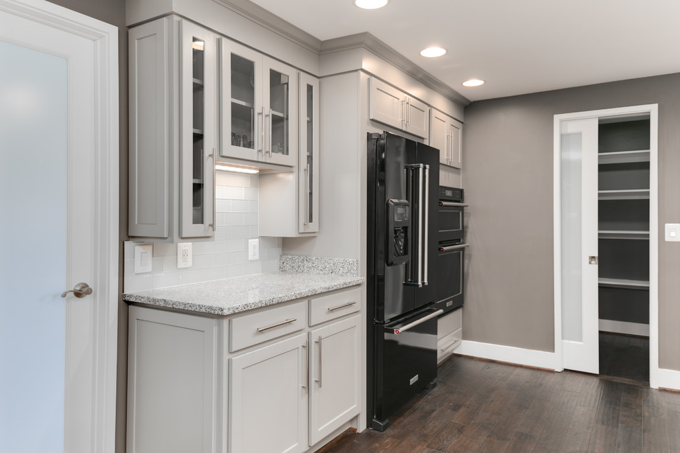Kitchen pantry - mid-sized transitional u-shaped dark wood floor kitchen pantry idea in DC Metro with an undermount sink, shaker cabinets, gray cabinets, granite countertops, white backsplash, glass tile backsplash, black appliances and an island