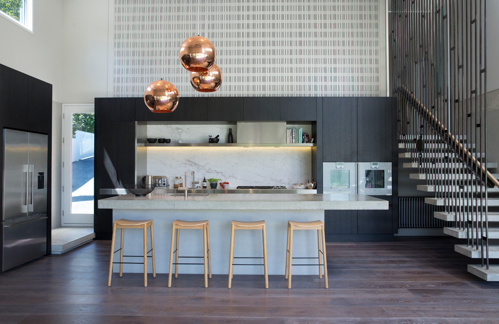 Moderne Küche in L-Form mit flächenbündigen Schrankfronten, schwarzen Schränken, Küchenrückwand in Weiß, Rückwand aus Stein, braunem Holzboden, Kücheninsel und Küchengeräten aus Edelstahl in Auckland