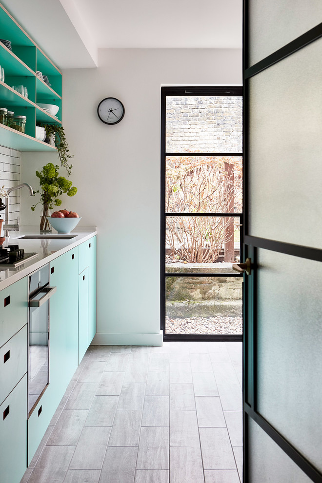 Photo of a medium sized scandi l-shaped kitchen/diner in London with a submerged sink, flat-panel cabinets, turquoise cabinets, composite countertops, white splashback, metro tiled splashback, integrated appliances, porcelain flooring, no island, grey floors and white worktops.