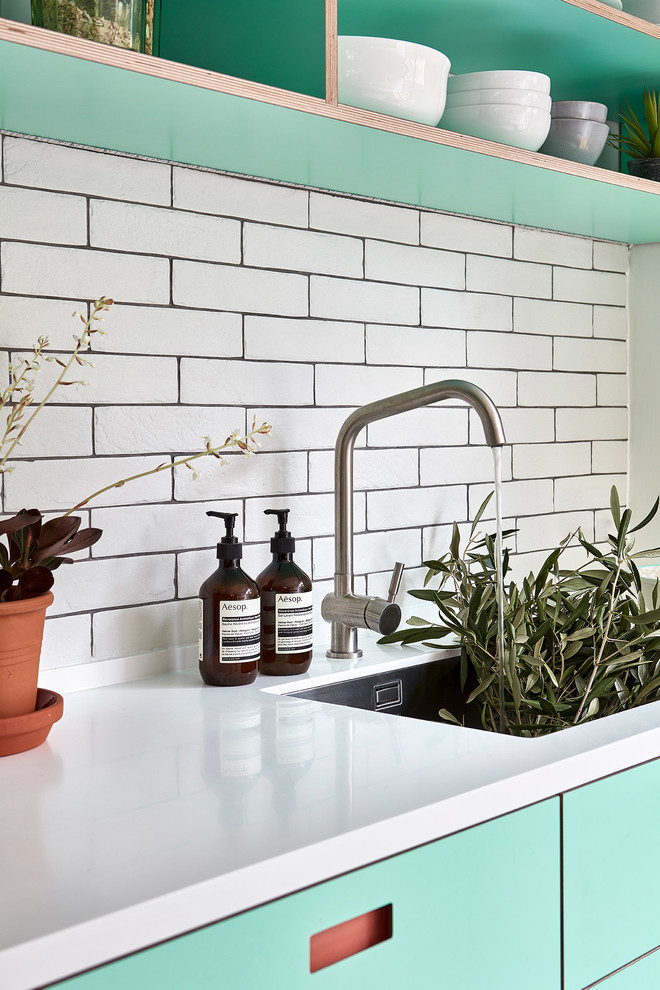 Example of a mid-sized danish l-shaped porcelain tile and gray floor eat-in kitchen design in London with an undermount sink, flat-panel cabinets, turquoise cabinets, solid surface countertops, white backsplash, subway tile backsplash, paneled appliances, no island and white countertops