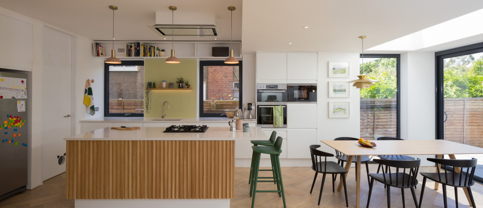 Example of a trendy galley medium tone wood floor and brown floor eat-in kitchen design in London with an undermount sink, flat-panel cabinets, white cabinets, stainless steel appliances and an island