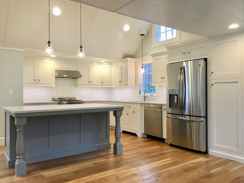 This is an example of a small traditional l-shaped kitchen/diner in Boston with a submerged sink, shaker cabinets, white cabinets, quartz worktops, white splashback, metro tiled splashback, stainless steel appliances, medium hardwood flooring, an island, brown floors and grey worktops.