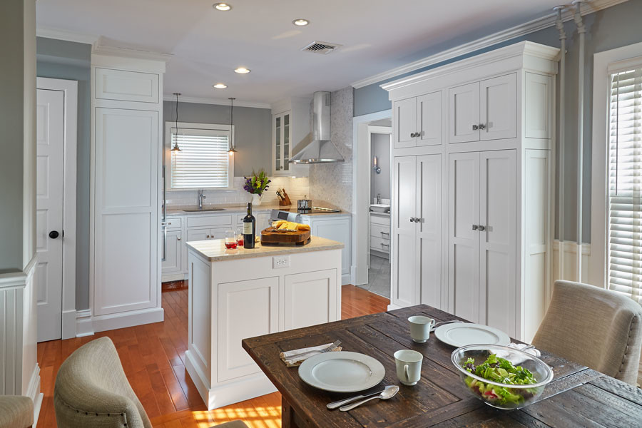 Foto på ett litet amerikanskt kök, med en undermonterad diskho, skåp i shakerstil, vita skåp, bänkskiva i kvarts, vitt stänkskydd, stänkskydd i porslinskakel, rostfria vitvaror, mellanmörkt trägolv och en köksö