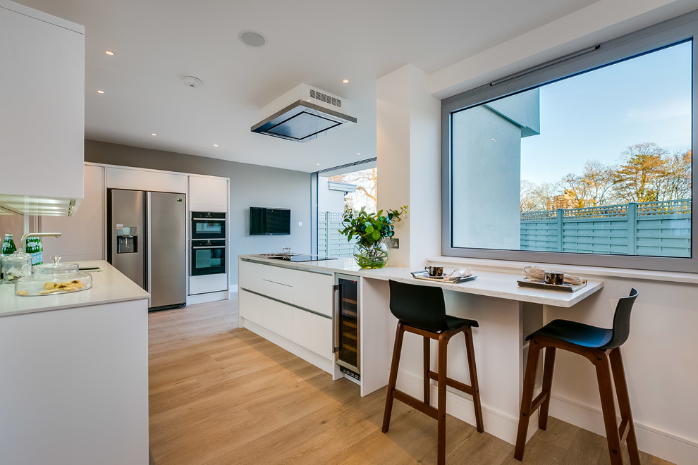 Große Moderne Wohnküche mit flächenbündigen Schrankfronten, weißen Schränken, Quarzit-Arbeitsplatte, braunem Holzboden und zwei Kücheninseln in London