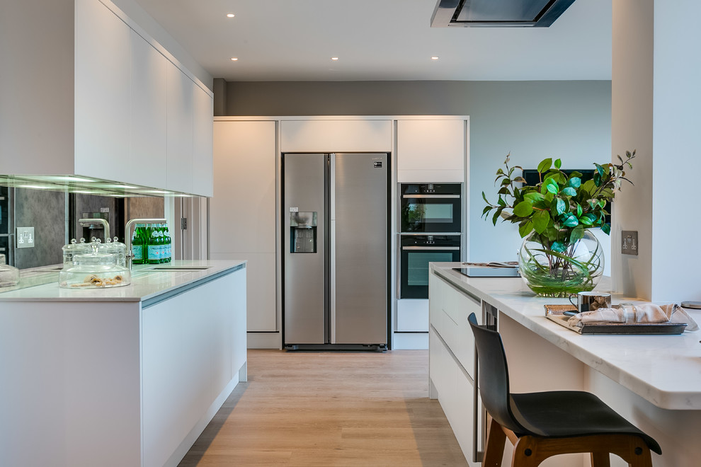 Photo of a large contemporary kitchen/diner in London with flat-panel cabinets, white cabinets, quartz worktops, medium hardwood flooring and multiple islands.