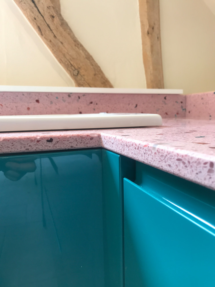 Bild på ett litet funkis rosa rosa kök, med släta luckor, blå skåp, bänkskiva i återvunnet glas och rostfria vitvaror
