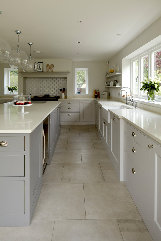 Inspiration for a large timeless u-shaped open concept kitchen remodel in Hertfordshire with a farmhouse sink, shaker cabinets, gray cabinets, quartzite countertops, white backsplash, subway tile backsplash, black appliances, an island and white countertops