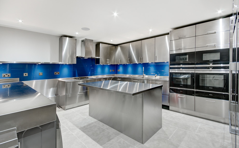 Kitchen - large traditional ceramic tile and gray floor kitchen idea in Hertfordshire with a double-bowl sink, flat-panel cabinets, stainless steel cabinets, stainless steel countertops, blue backsplash, black appliances and an island
