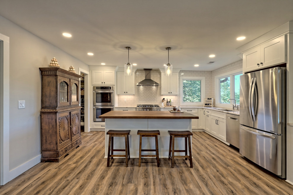 Inspiration for a mid-sized farmhouse l-shaped laminate floor and brown floor open concept kitchen remodel in Atlanta with an undermount sink, shaker cabinets, white cabinets, quartz countertops, white backsplash, subway tile backsplash, stainless steel appliances, an island and white countertops