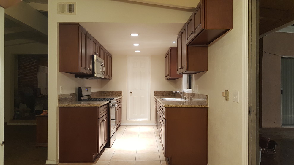 Photo of a small traditional galley kitchen with a built-in sink, raised-panel cabinets, dark wood cabinets, granite worktops, stainless steel appliances, no island, beige floors and brown worktops.