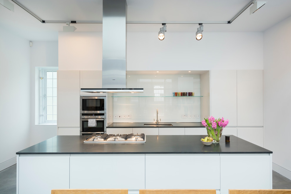 Inspiration for an expansive urban single-wall kitchen/diner in London with a built-in sink, flat-panel cabinets, composite countertops, white splashback, glass tiled splashback, stainless steel appliances, concrete flooring and an island.
