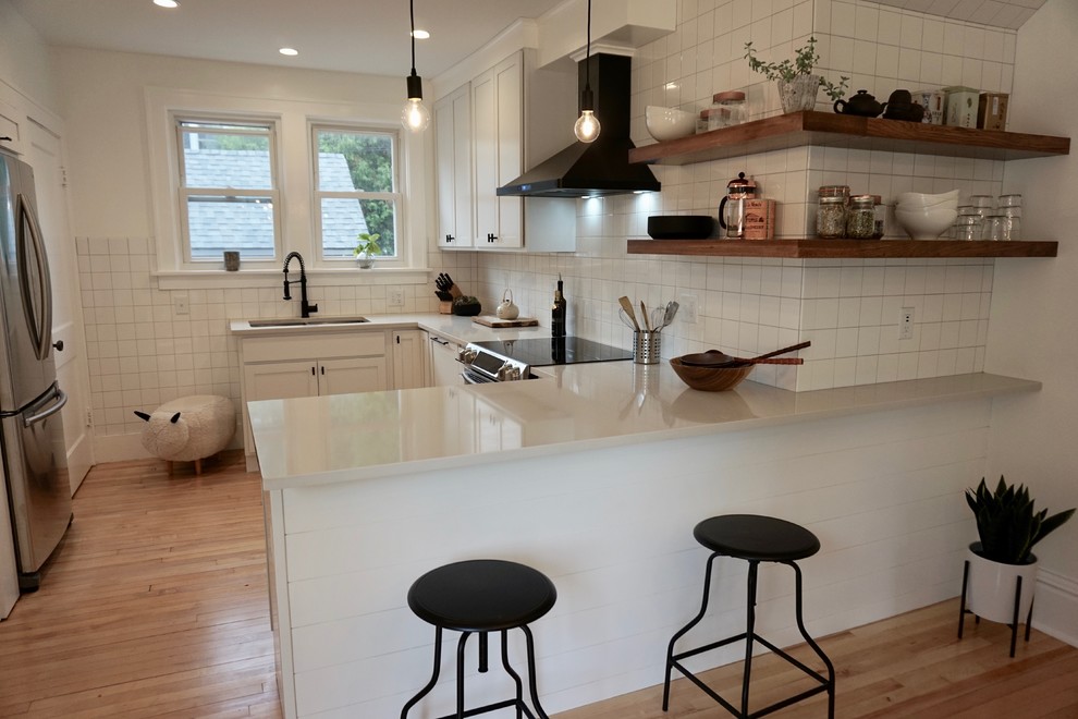 Photo of a small scandinavian u-shaped kitchen/diner in Charleston with a submerged sink, shaker cabinets, white cabinets, engineered stone countertops, white splashback, ceramic splashback, stainless steel appliances, light hardwood flooring, a breakfast bar, beige floors and white worktops.