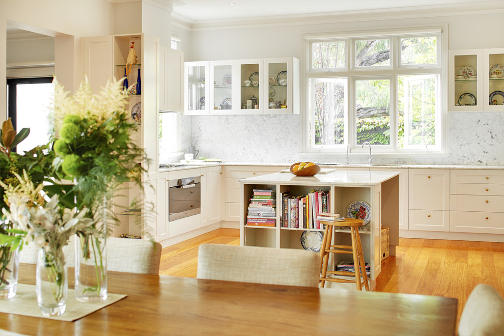 Bild på ett vintage grå grått kök, med en undermonterad diskho, skåp i shakerstil, vita skåp, marmorbänkskiva, grått stänkskydd, stänkskydd i marmor, vita vitvaror, mellanmörkt trägolv och en köksö