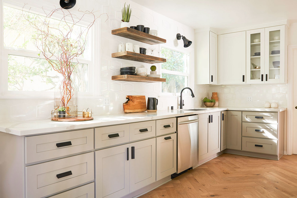 Cette photo montre une cuisine chic en L avec un évier encastré, un placard à porte shaker, des portes de placard beiges, une crédence blanche, un électroménager en acier inoxydable, un sol en bois brun, un sol marron et un plan de travail blanc.