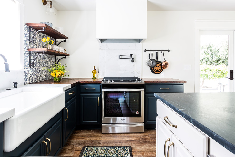 Lantlig inredning av ett mellanstort brun brunt kök, med en rustik diskho, luckor med upphöjd panel, blå skåp, träbänkskiva, blått stänkskydd, stänkskydd i cementkakel, rostfria vitvaror, laminatgolv, en köksö och brunt golv
