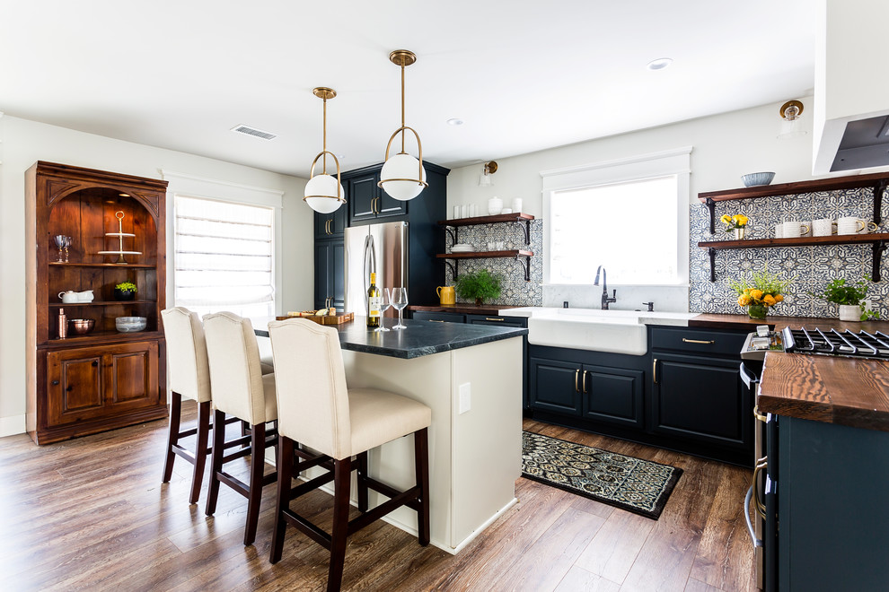 Foto på ett mellanstort lantligt brun kök, med en rustik diskho, luckor med upphöjd panel, blå skåp, träbänkskiva, blått stänkskydd, stänkskydd i cementkakel, rostfria vitvaror, laminatgolv, en köksö och brunt golv