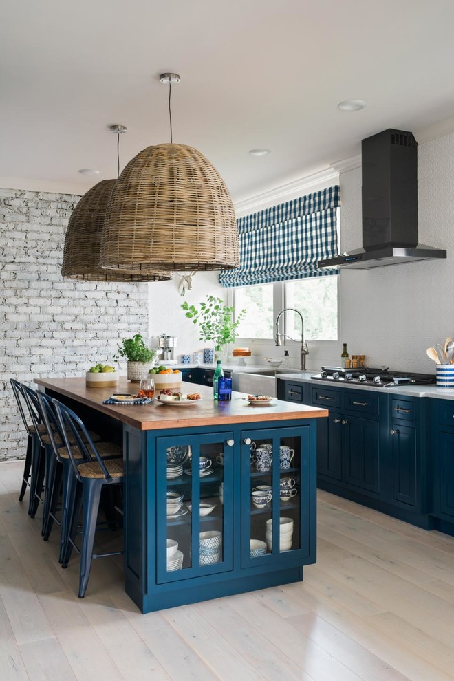 Photo of a classic kitchen in Atlanta with blue cabinets, light hardwood flooring, a belfast sink, glass-front cabinets, wood worktops, window splashback, an island and beige floors.
