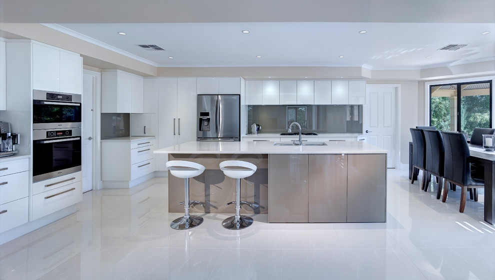 Foto di un'ampia cucina minimal con lavello sottopiano, ante bianche, paraspruzzi grigio, paraspruzzi con lastra di vetro e elettrodomestici in acciaio inossidabile