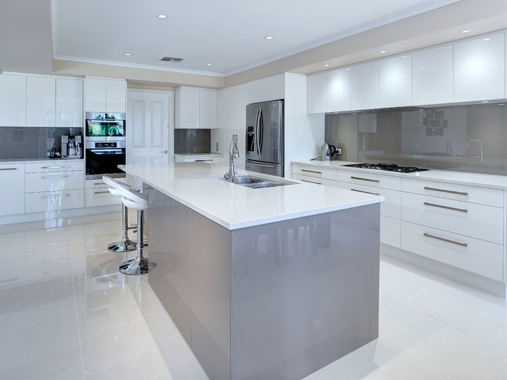 Immagine di un'ampia cucina contemporanea con lavello sottopiano, ante bianche, paraspruzzi grigio, paraspruzzi con lastra di vetro e elettrodomestici in acciaio inossidabile