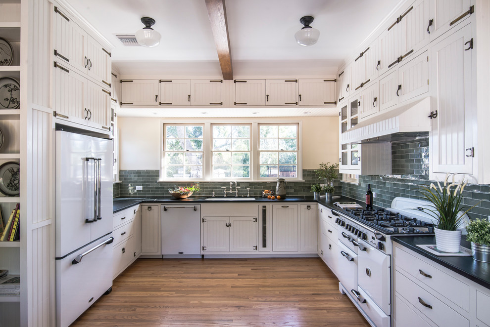 Klassische Küche ohne Insel in U-Form mit Unterbauwaschbecken, Schrankfronten mit vertiefter Füllung, Küchenrückwand in Grau, weißen Elektrogeräten und braunem Holzboden in Los Angeles
