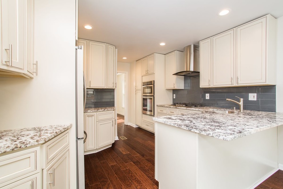 Inspiration for a mid-sized timeless u-shaped medium tone wood floor and brown floor kitchen remodel in DC Metro with an undermount sink, recessed-panel cabinets, white cabinets, granite countertops, gray backsplash, glass tile backsplash, stainless steel appliances, a peninsula and white countertops