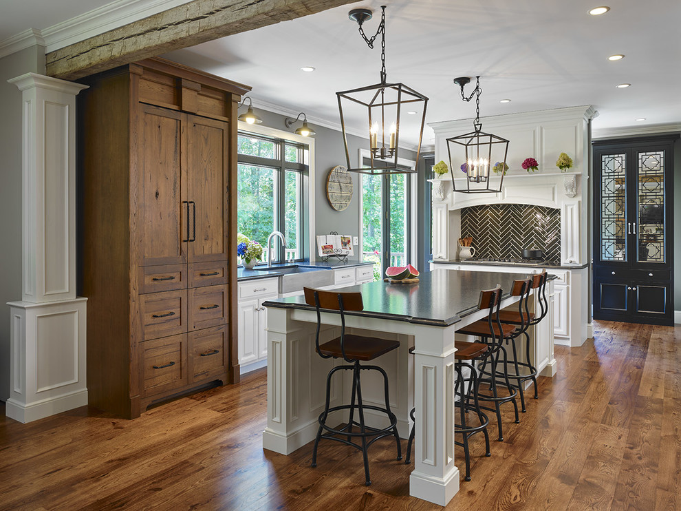 Exempel på ett mellanstort klassiskt l-kök, med en rustik diskho, mellanmörkt trägolv, en köksö, luckor med upphöjd panel, vita skåp, svart stänkskydd, stänkskydd i glaskakel och rostfria vitvaror