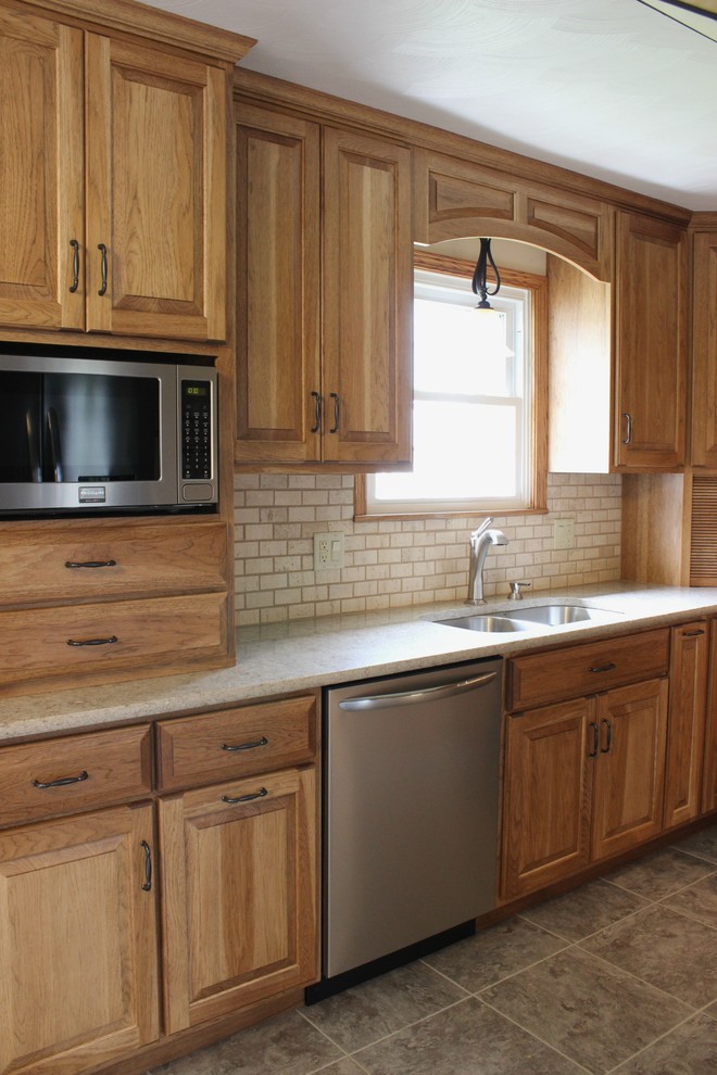 Bild på ett mellanstort lantligt kök, med en undermonterad diskho, luckor med upphöjd panel, skåp i mellenmörkt trä, bänkskiva i kvarts, beige stänkskydd, stänkskydd i stenkakel, rostfria vitvaror och vinylgolv