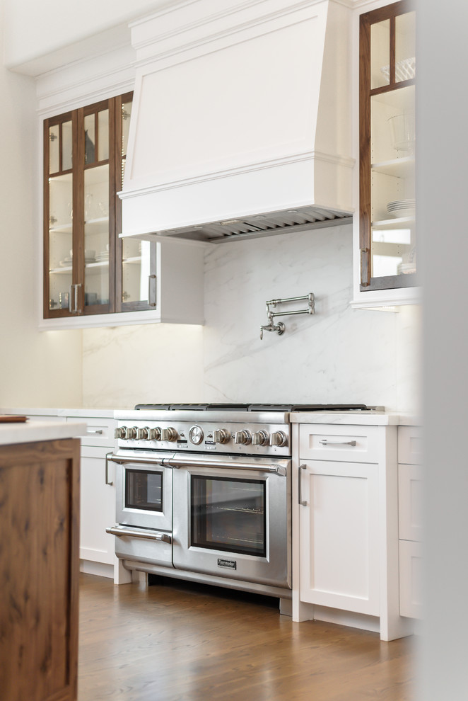 Bild på ett vintage kök, med en rustik diskho, släta luckor, vita skåp, marmorbänkskiva, vitt stänkskydd, stänkskydd i marmor, rostfria vitvaror, ljust trägolv och en köksö