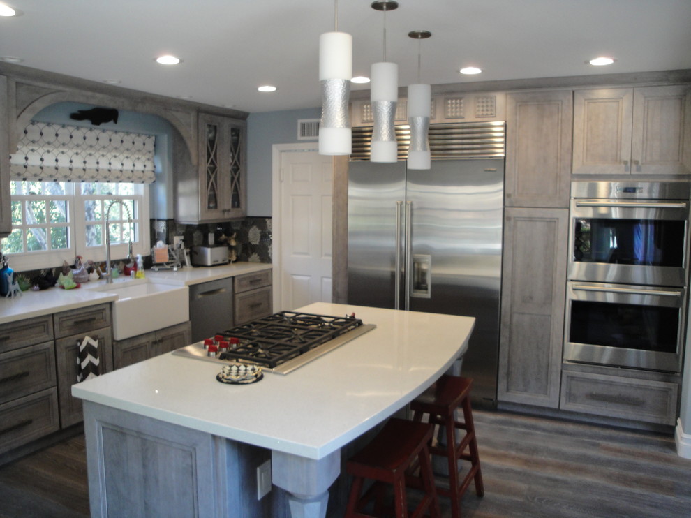 Inredning av ett lantligt mellanstort vit vitt kök, med en rustik diskho, luckor med infälld panel, skåp i slitet trä, bänkskiva i kvartsit, flerfärgad stänkskydd, stänkskydd i mosaik, rostfria vitvaror, mörkt trägolv, en köksö och brunt golv