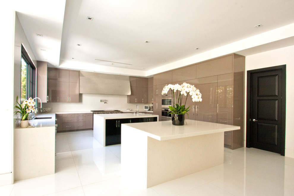 Example of a huge minimalist u-shaped marble floor eat-in kitchen design in Los Angeles with an undermount sink, flat-panel cabinets, beige cabinets, solid surface countertops, stainless steel appliances and two islands