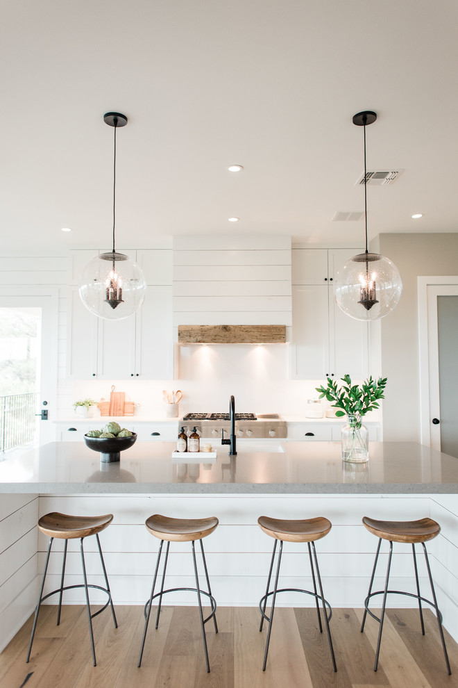 Example of a large transitional u-shaped light wood floor and brown floor open concept kitchen design in Austin with a farmhouse sink, shaker cabinets, white cabinets, quartzite countertops, white backsplash, stone slab backsplash, stainless steel appliances, an island and gray countertops