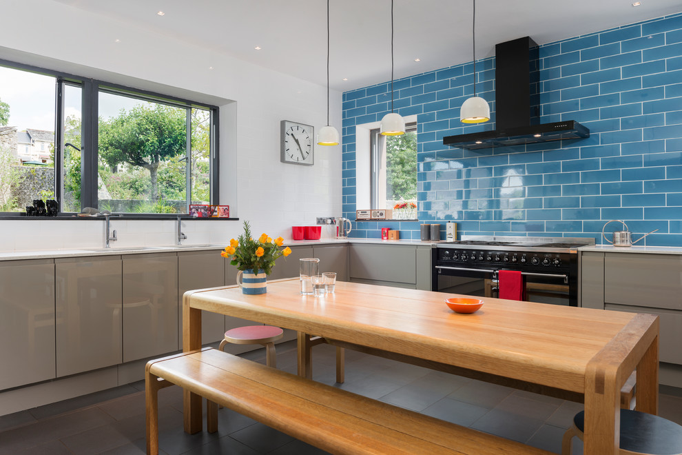 Стильный дизайн: угловая, глянцевая кухня в современном стиле с обеденным столом, плоскими фасадами, серыми фасадами, синим фартуком, фартуком из плитки кабанчик и черной техникой - последний тренд
