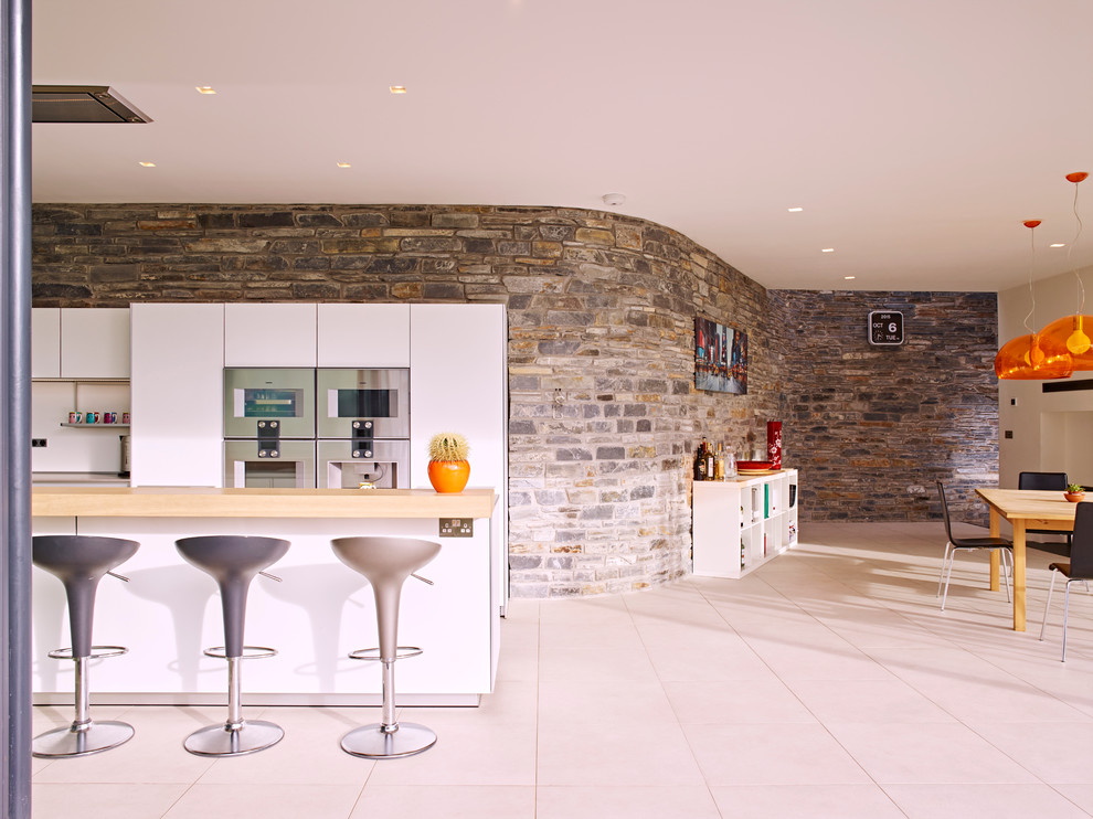 Photo of a medium sized contemporary single-wall kitchen/diner in Devon with an integrated sink, flat-panel cabinets, white cabinets, composite countertops, white splashback, stainless steel appliances, ceramic flooring and an island.