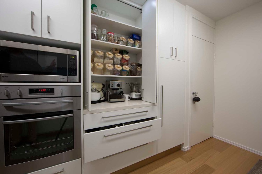 Exempel på ett mellanstort modernt vit vitt kök, med en nedsänkt diskho, släta luckor, vita skåp, bänkskiva i kvarts, blått stänkskydd, rostfria vitvaror och mellanmörkt trägolv