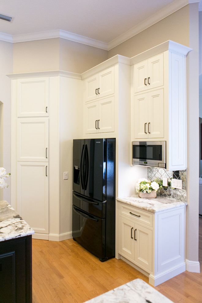 Bild på ett mellanstort vintage kök, med en undermonterad diskho, luckor med infälld panel, vita skåp, granitbänkskiva, spegel som stänkskydd, svarta vitvaror, ljust trägolv, en köksö och brunt golv