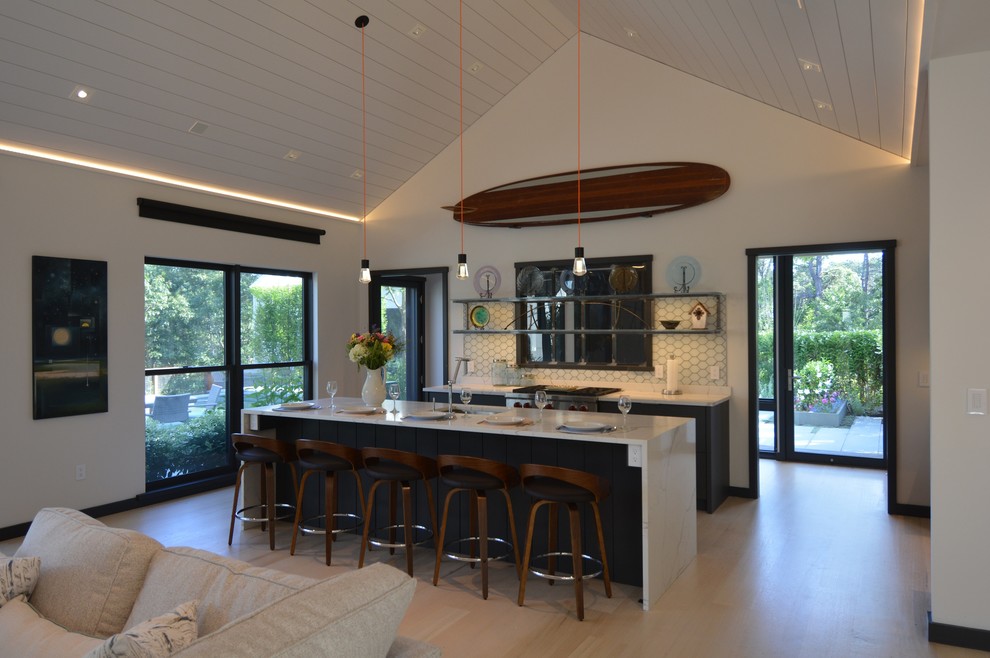 This is an example of a medium sized beach style u-shaped kitchen/diner in Boston with a submerged sink, flat-panel cabinets, blue cabinets, engineered stone countertops, white splashback, ceramic splashback, stainless steel appliances, light hardwood flooring, an island, beige floors and white worktops.