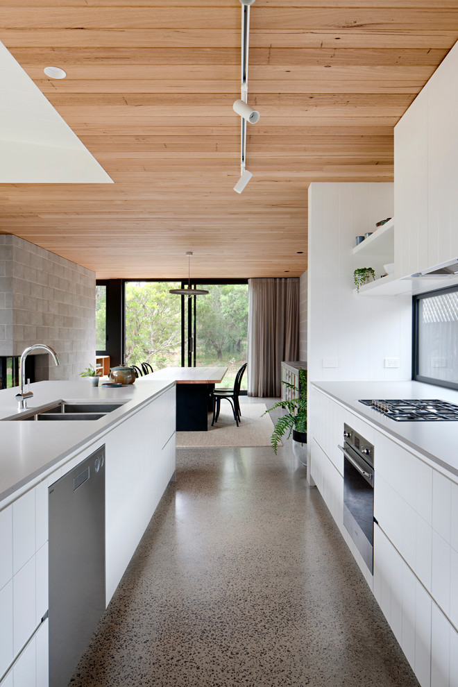 Idée de décoration pour une cuisine ouverte parallèle design avec un évier 2 bacs, un placard à porte plane, des portes de placard blanches, un électroménager en acier inoxydable, sol en béton ciré et un sol gris.