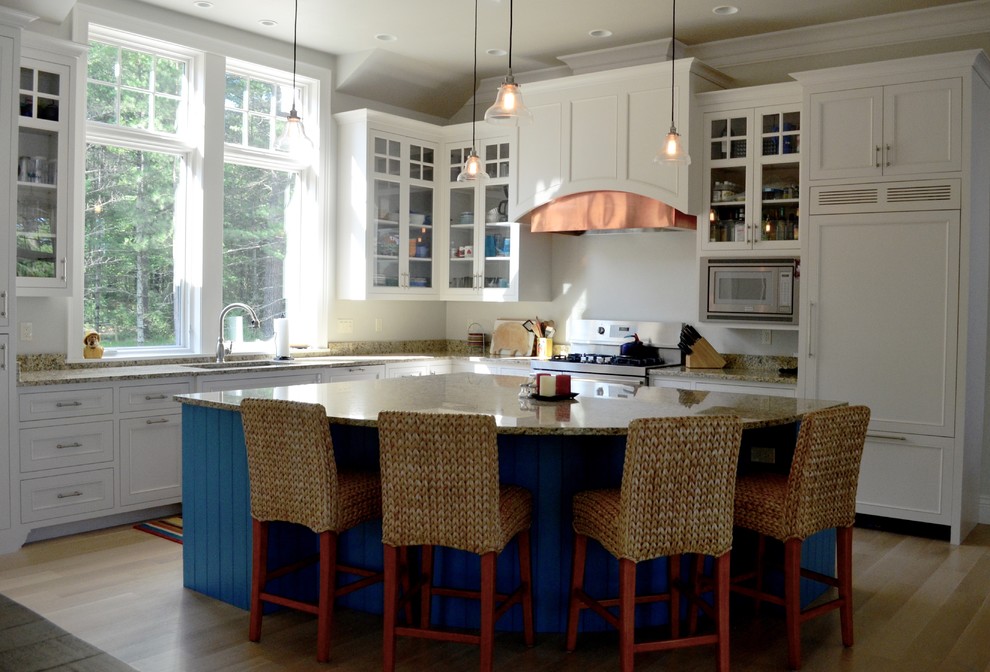 This is an example of a beach style l-shaped open plan kitchen in Other with a submerged sink, flat-panel cabinets, white cabinets, granite worktops, integrated appliances, light hardwood flooring and an island.
