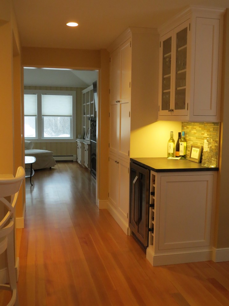 Example of a mid-sized beach style l-shaped medium tone wood floor eat-in kitchen design in Portland Maine with beaded inset cabinets, white cabinets, granite countertops, multicolored backsplash, stone tile backsplash, stainless steel appliances and an island