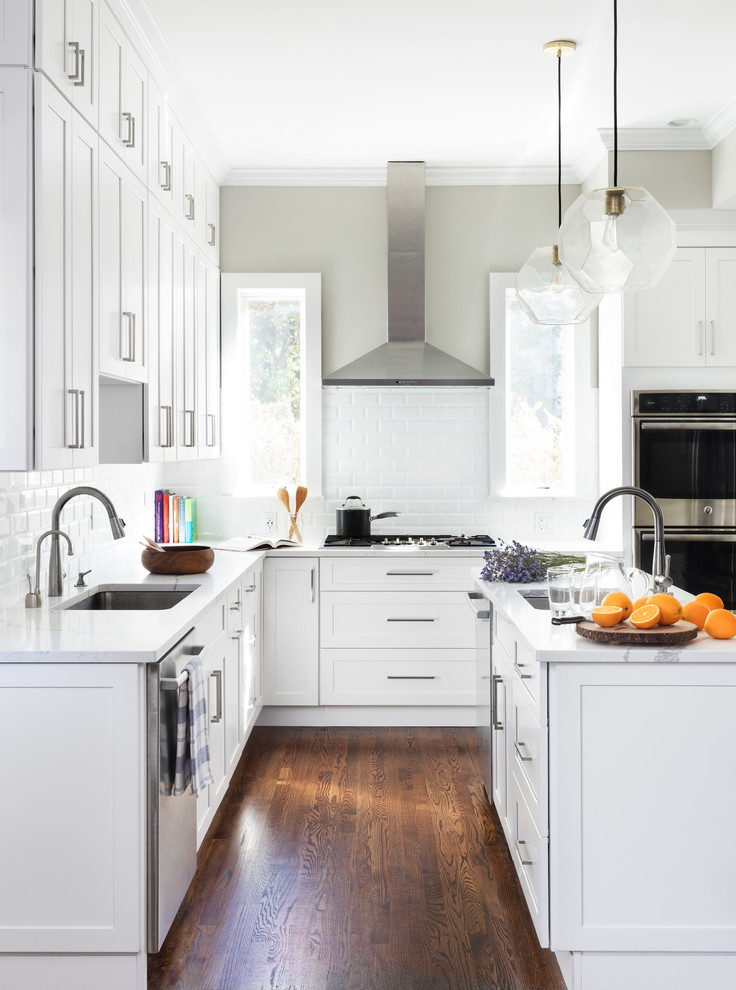 Small trendy u-shaped medium tone wood floor and brown floor open concept kitchen photo in New York with a drop-in sink, shaker cabinets, white cabinets, quartz countertops, white backsplash, ceramic backsplash, stainless steel appliances, an island and white countertops