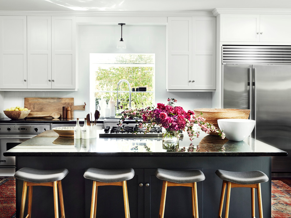 This is an example of a traditional u-shaped kitchen in Los Angeles with shaker cabinets, white cabinets, white splashback, metro tiled splashback, stainless steel appliances and an island.