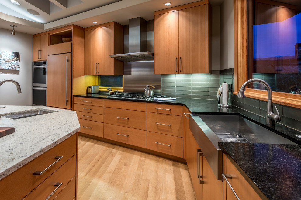 Example of a mid-sized trendy l-shaped light wood floor open concept kitchen design in Portland with a farmhouse sink, flat-panel cabinets, medium tone wood cabinets, granite countertops, gray backsplash, glass tile backsplash, stainless steel appliances and an island