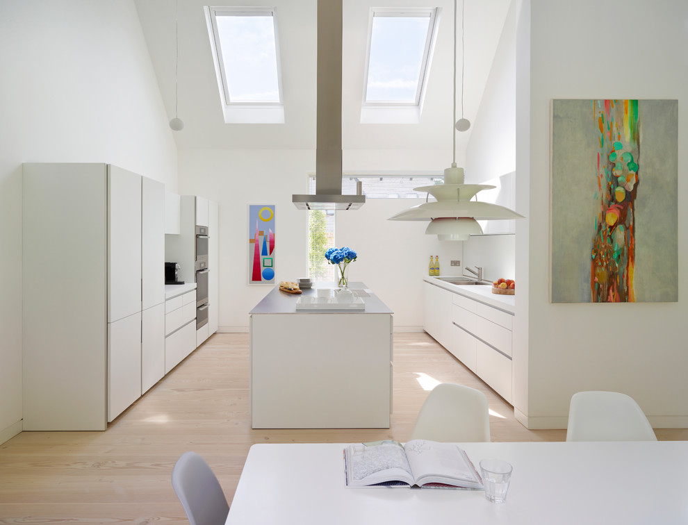Zweizeilige Moderne Wohnküche mit Doppelwaschbecken, flächenbündigen Schrankfronten, weißen Schränken, Küchenrückwand in Weiß, Küchengeräten aus Edelstahl, hellem Holzboden und Kücheninsel in Oxfordshire