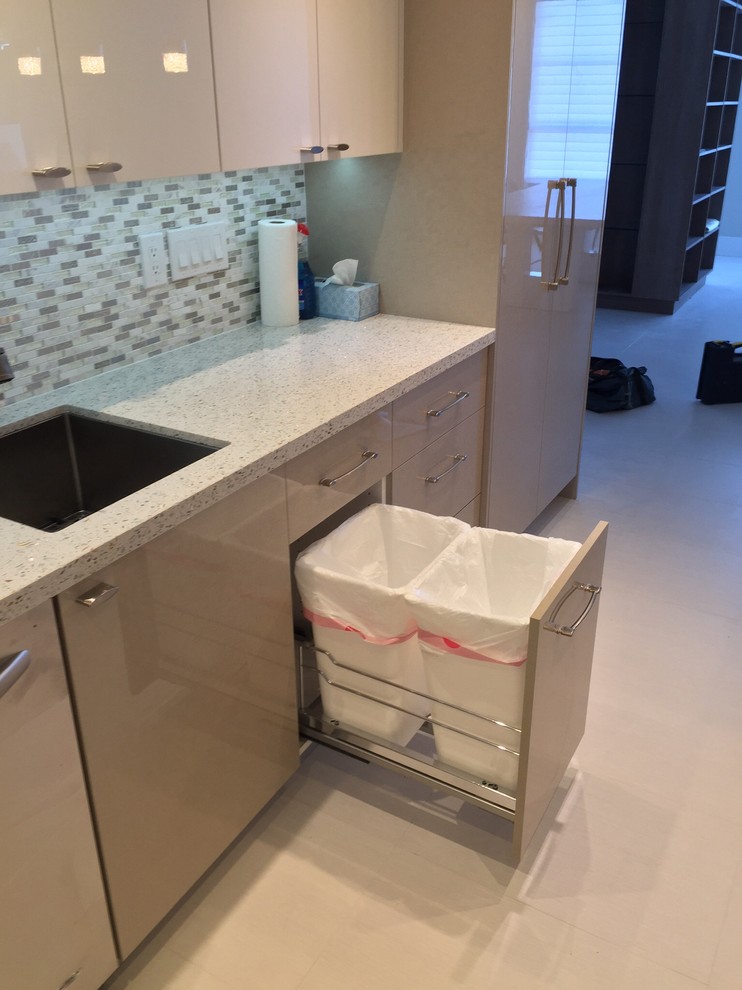 Photo of a medium sized modern u-shaped kitchen pantry in Miami with a submerged sink, flat-panel cabinets, white cabinets, recycled glass countertops, grey splashback, glass tiled splashback, stainless steel appliances, porcelain flooring and a breakfast bar.