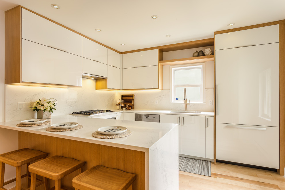 Modern inredning av ett mellanstort kök, med en undermonterad diskho, släta luckor, vita skåp, bänkskiva i kvarts, vitt stänkskydd, stänkskydd i sten, integrerade vitvaror, ljust trägolv, en halv köksö och brunt golv