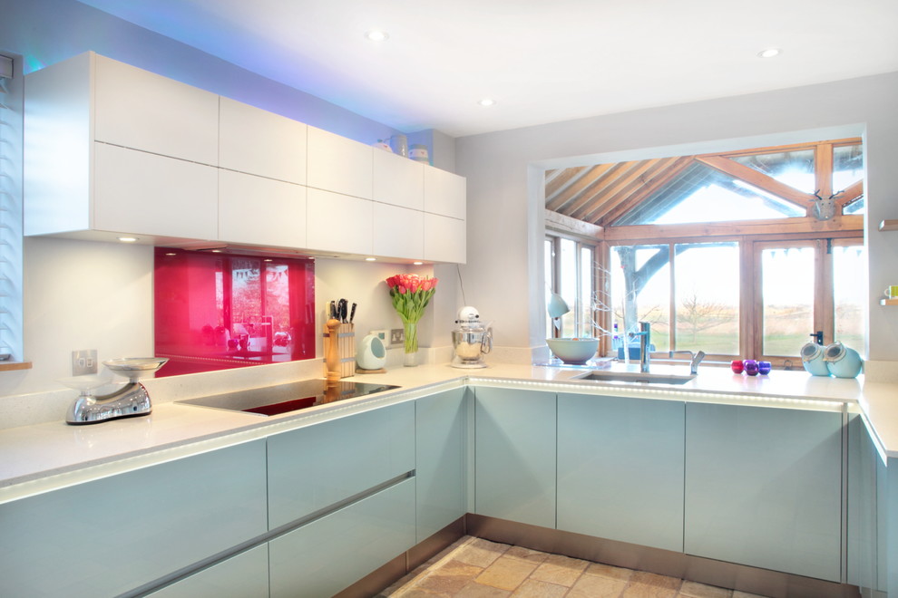Photo of a large contemporary u-shaped open plan kitchen in Buckinghamshire with red splashback, stainless steel appliances, a breakfast bar, an integrated sink, flat-panel cabinets, blue cabinets, quartz worktops, glass sheet splashback and laminate floors.
