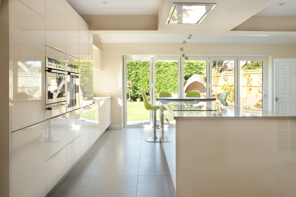 This is an example of a large modern single-wall kitchen/diner in Buckinghamshire with a submerged sink, flat-panel cabinets, quartz worktops, stainless steel appliances, porcelain flooring, an island and white cabinets.